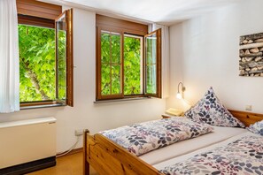 A bedroom with two beds, a radiator, and a window with a view of greenery.