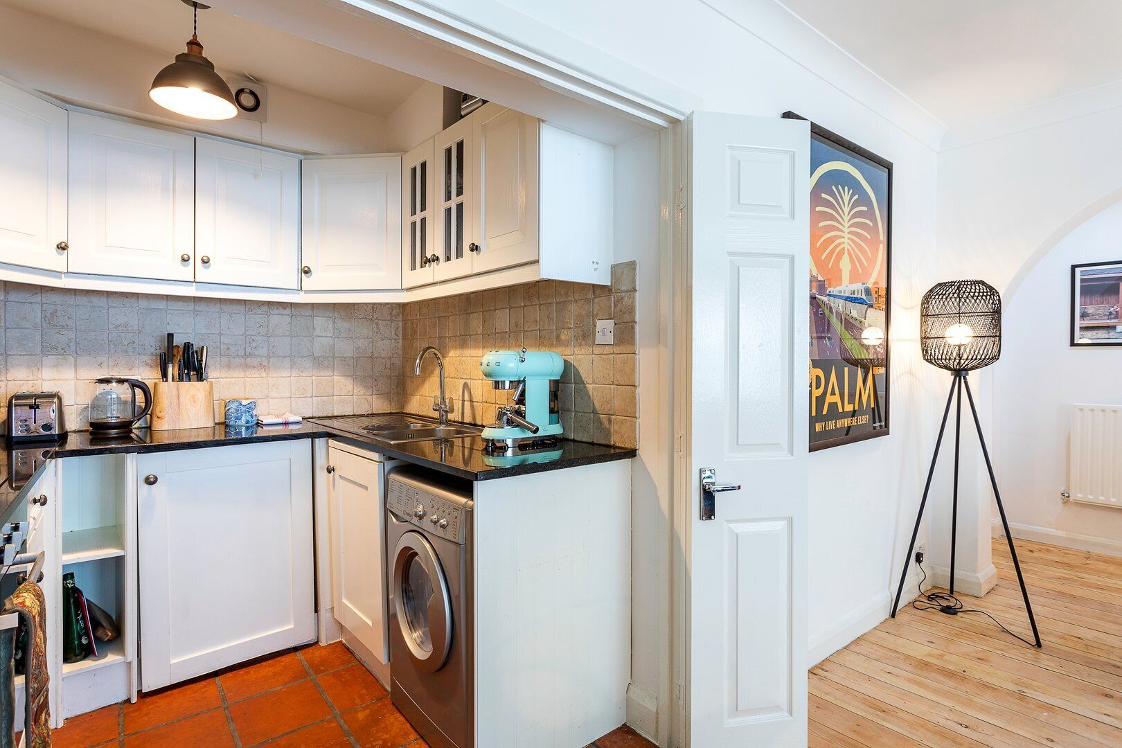 Une cuisine moderne avec des meubles blancs, un lave-linge, une machine à café et un lampadaire.