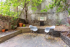 A courtyard with brick walls, two white chairs, and potted plants. - Quaint Fulham Retreat: Cozy 1-bedroom Pied-à-terre (London)