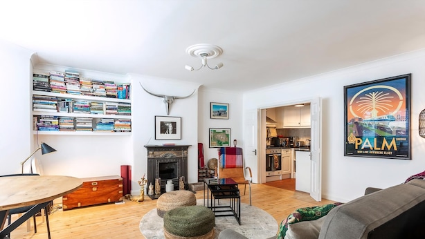 Una sala de estar con chimenea, estanterías, una mesa de comedor y una cocina visible a través de una puerta abierta.