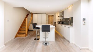 Een moderne keuken met een centraal eiland, een houten trap en witte kasten.