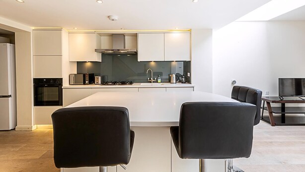 Een moderne keuken met witte kasten, een centraal eiland en een eethoek met zwarte stoelen.