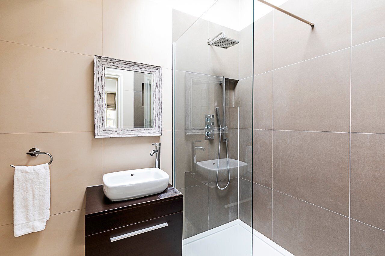 Un baño moderno con ducha de vidrio, lavamanos blanco y espejo con marco envejecido.