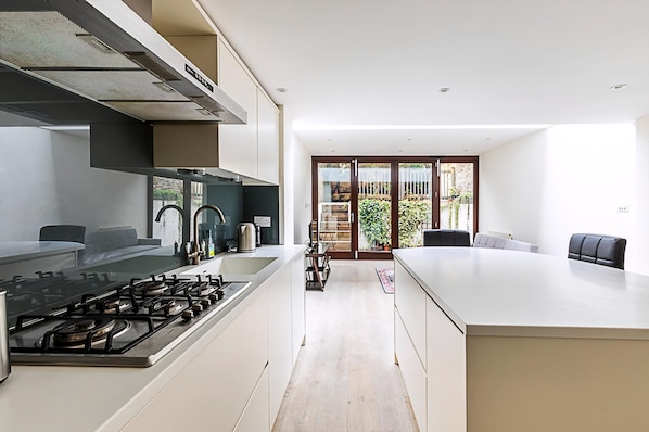A modern kitchen with a gas stove, a range hood, and a dining area with a table and chairs. - Beautiful Modern 4BR House in Central London (London)