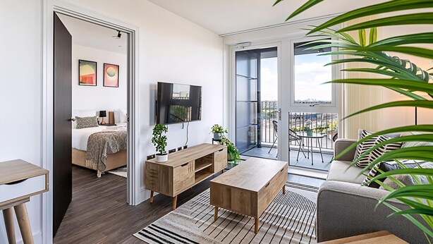 Una sala de estar moderna con sofá, mesa de centro, televisor y un balcón con vistas a la ciudad.