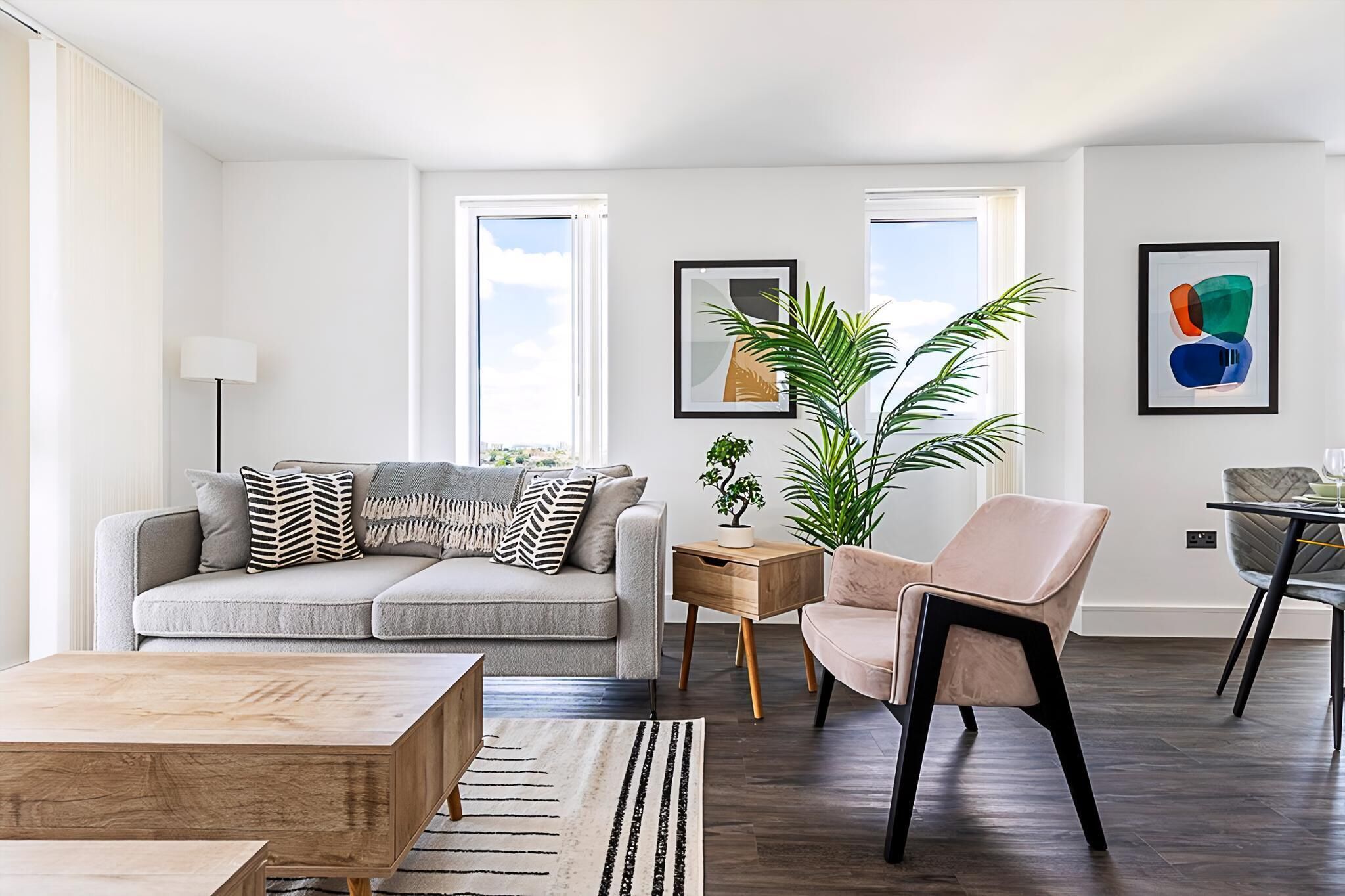 En moderne stue med en grå sofa, et træ sofabord, en beige lænestol og et lille sofabord med en plante.