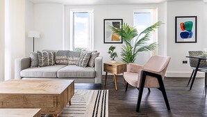 Una sala de estar moderna con un sofá gris, una mesa de centro de madera, un sillón beige y una mesita auxiliar con una planta.
