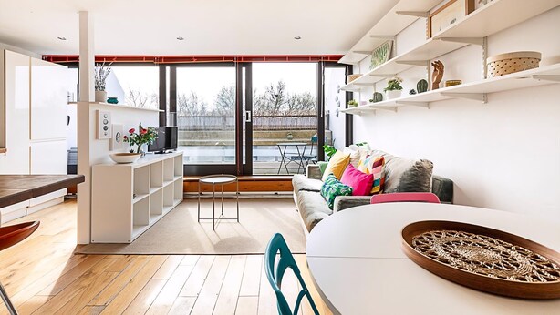 A modern living space with a kitchen, dining area, and a sofa with colorful cushions.