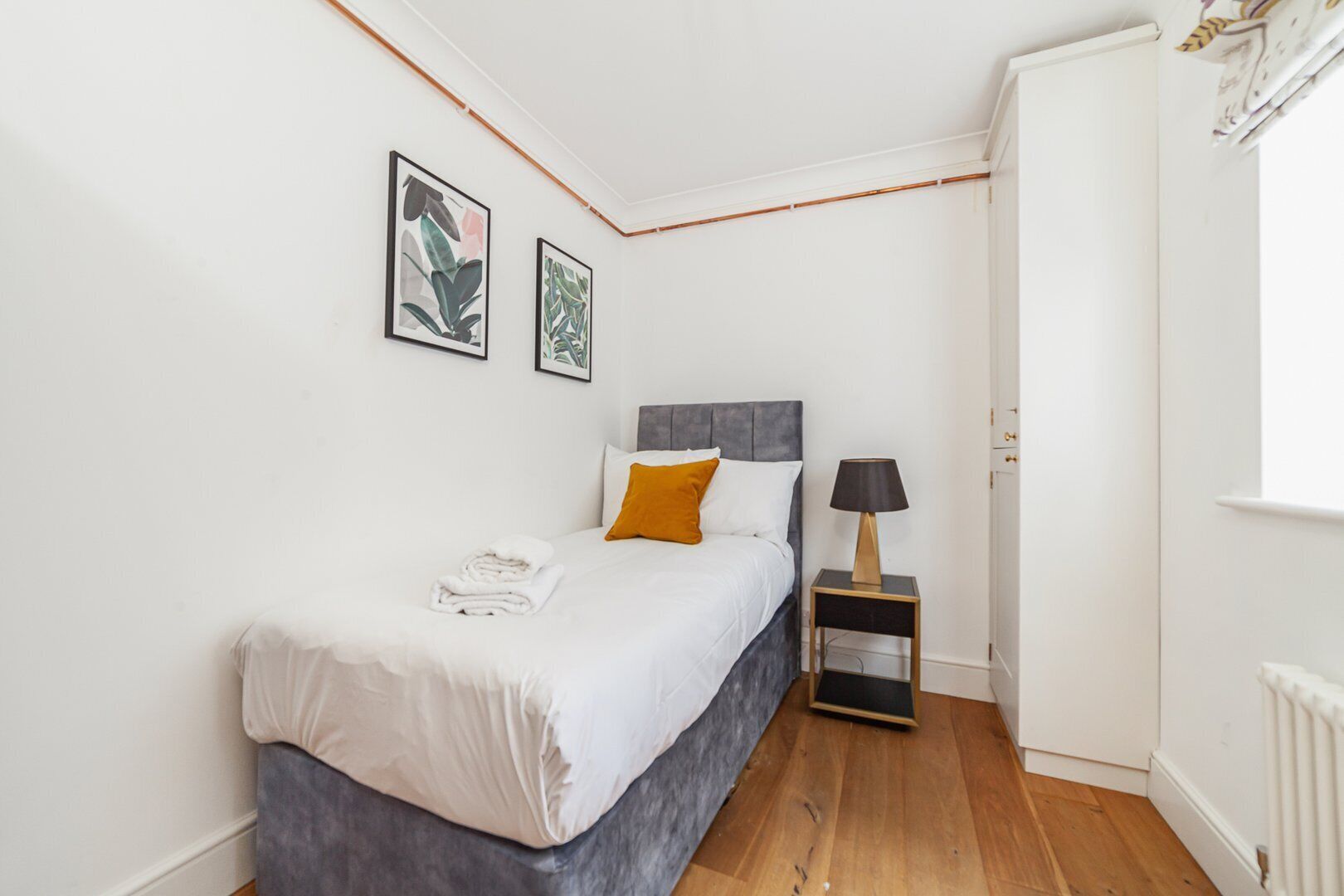 Een slaapkamer met een bed, een nachtkastje en twee foto's in lijsten aan de muur.