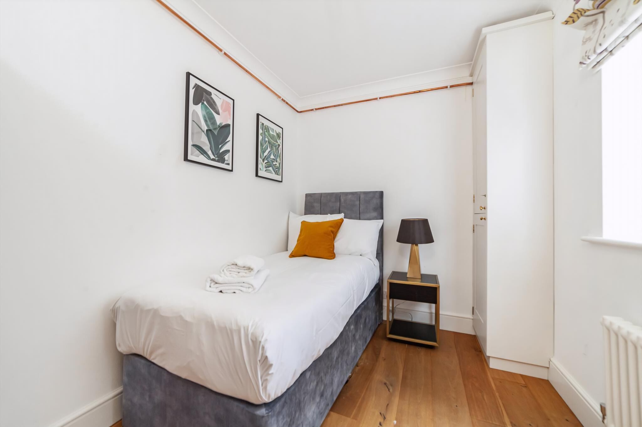 A bedroom with a bed, a nightstand, a lamp, and two framed pictures on the wall.