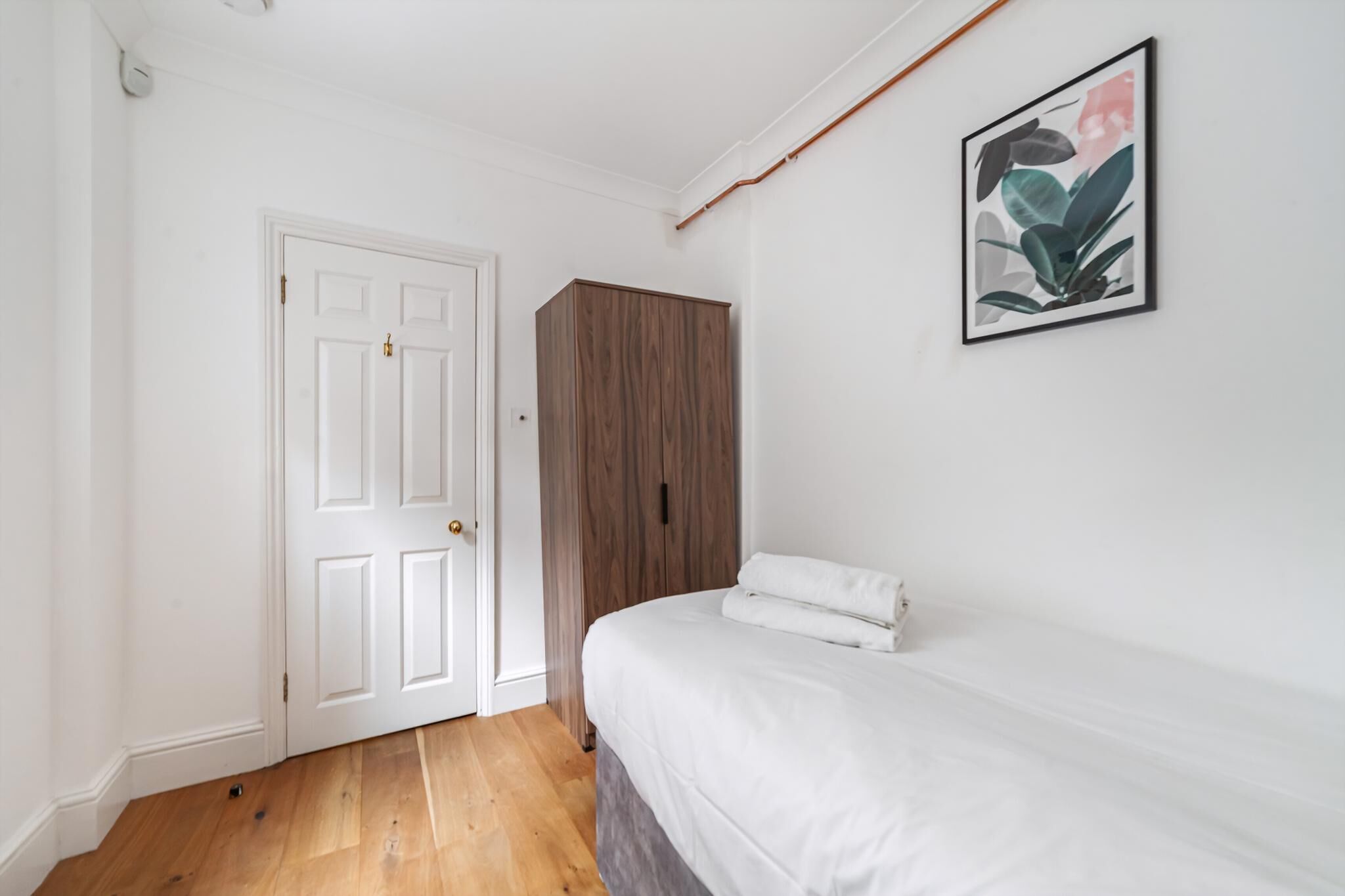 Ein Schlafzimmer mit einem Holzschrank, einer weißen Tür und einem gerahmten Bild an der Wand.