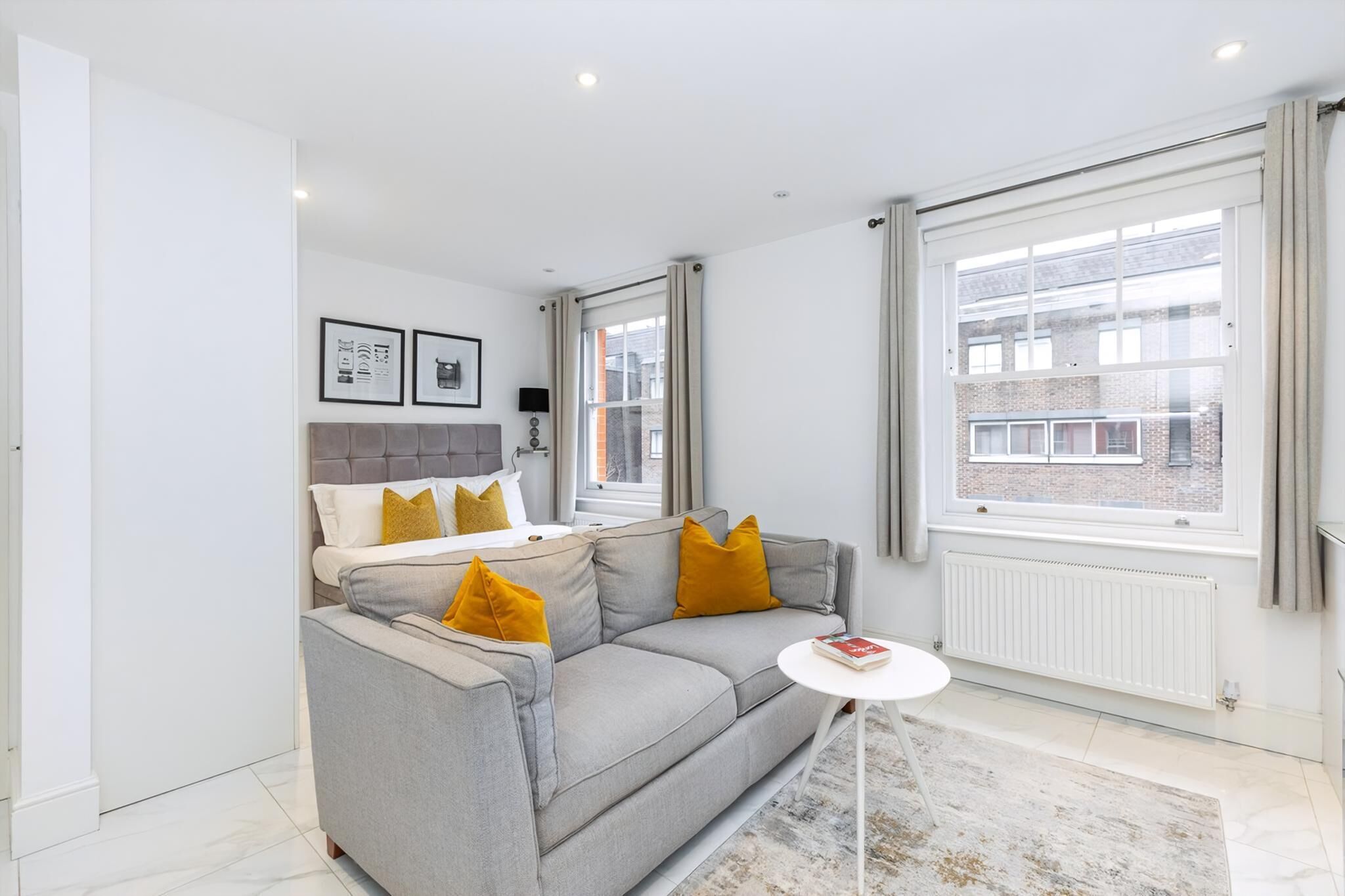 A modern living room with a grey sofa, a small white table, and a large window with curtains.