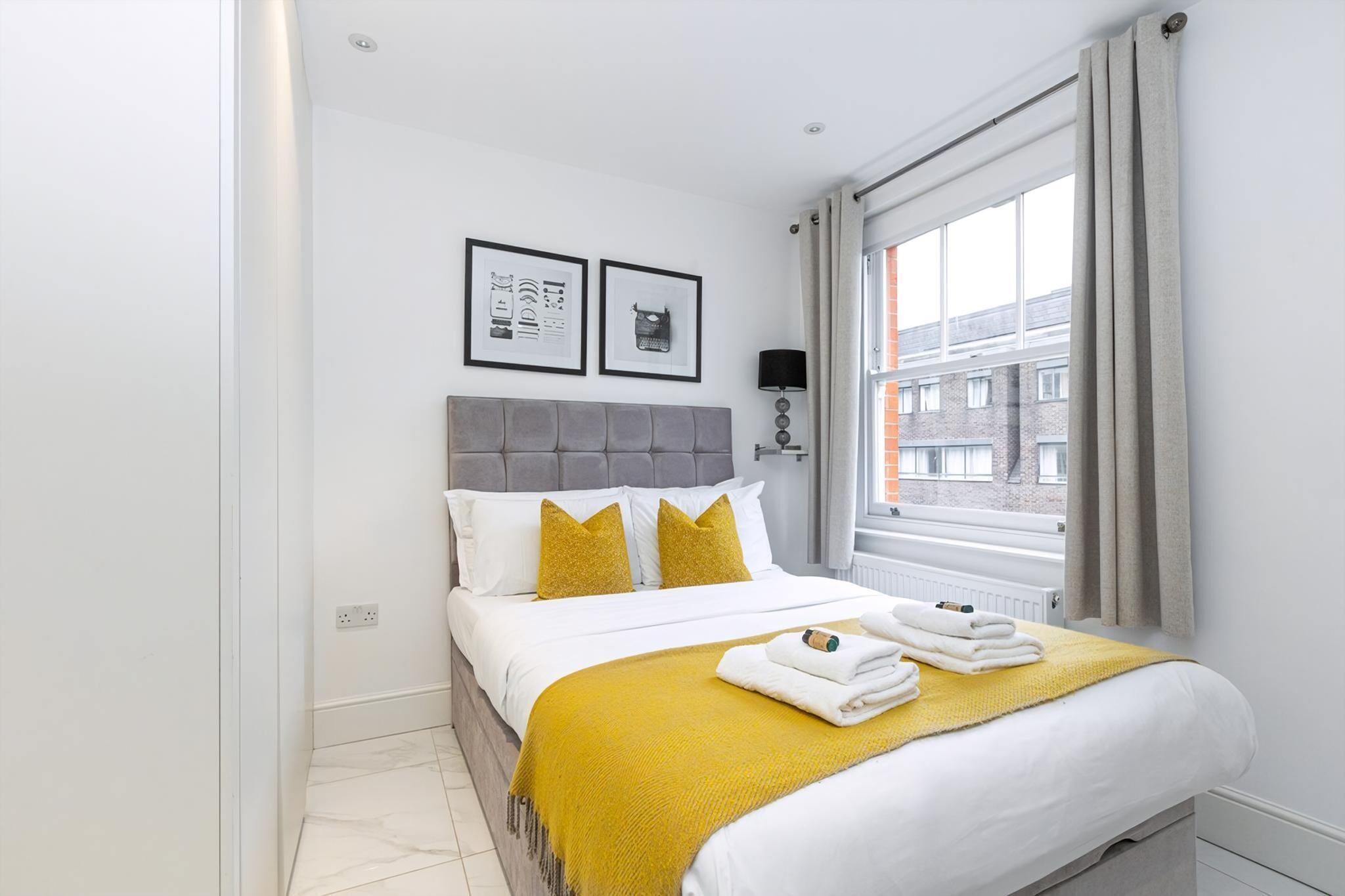 A hotel room with a bed, a window with curtains, a headboard, and two framed pictures on the wall.