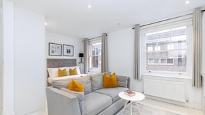 Una sala de estar moderna con un sofá gris, una mesita blanca y un ventanal con cortinas.