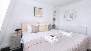 A neatly arranged bedroom with a bed, bedside tables, a framed picture, and a round mirror.