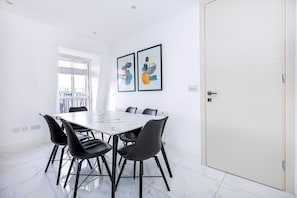 Un espace repas moderne avec une table en marbre, des chaises noires et une œuvre d’art abstrait accrochée au mur.