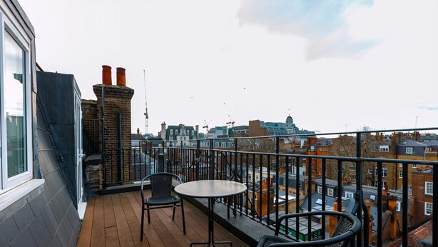 A balcony with a table and chairs, overlooking a cityscape with buildings and a crane.