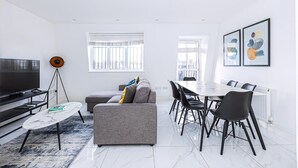 A modern living room with a sofa, dining table, chairs, a TV, and artwork on the walls.