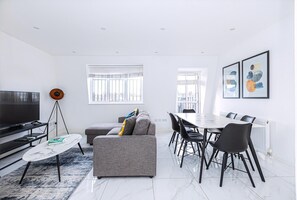 Uma sala de estar moderna com sofá, mesa de jantar, cadeiras, televisão e obras de arte nas paredes.