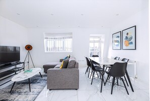 Un salon moderne comprenant un canapé, une table à manger, des chaises, un téléviseur et des œuvres d’art accrochées aux murs.