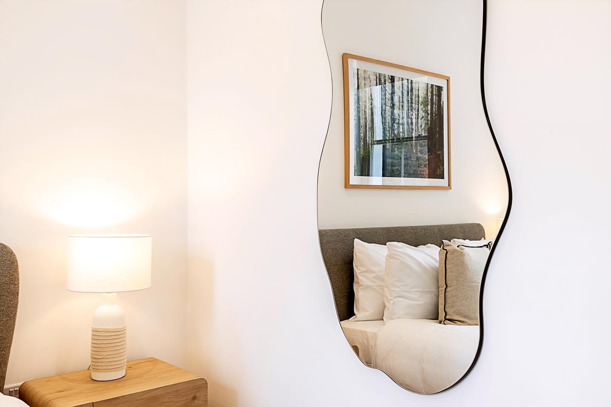 A bedroom with a bed, a bedside table with a lamp, and a large mirror on the wall.