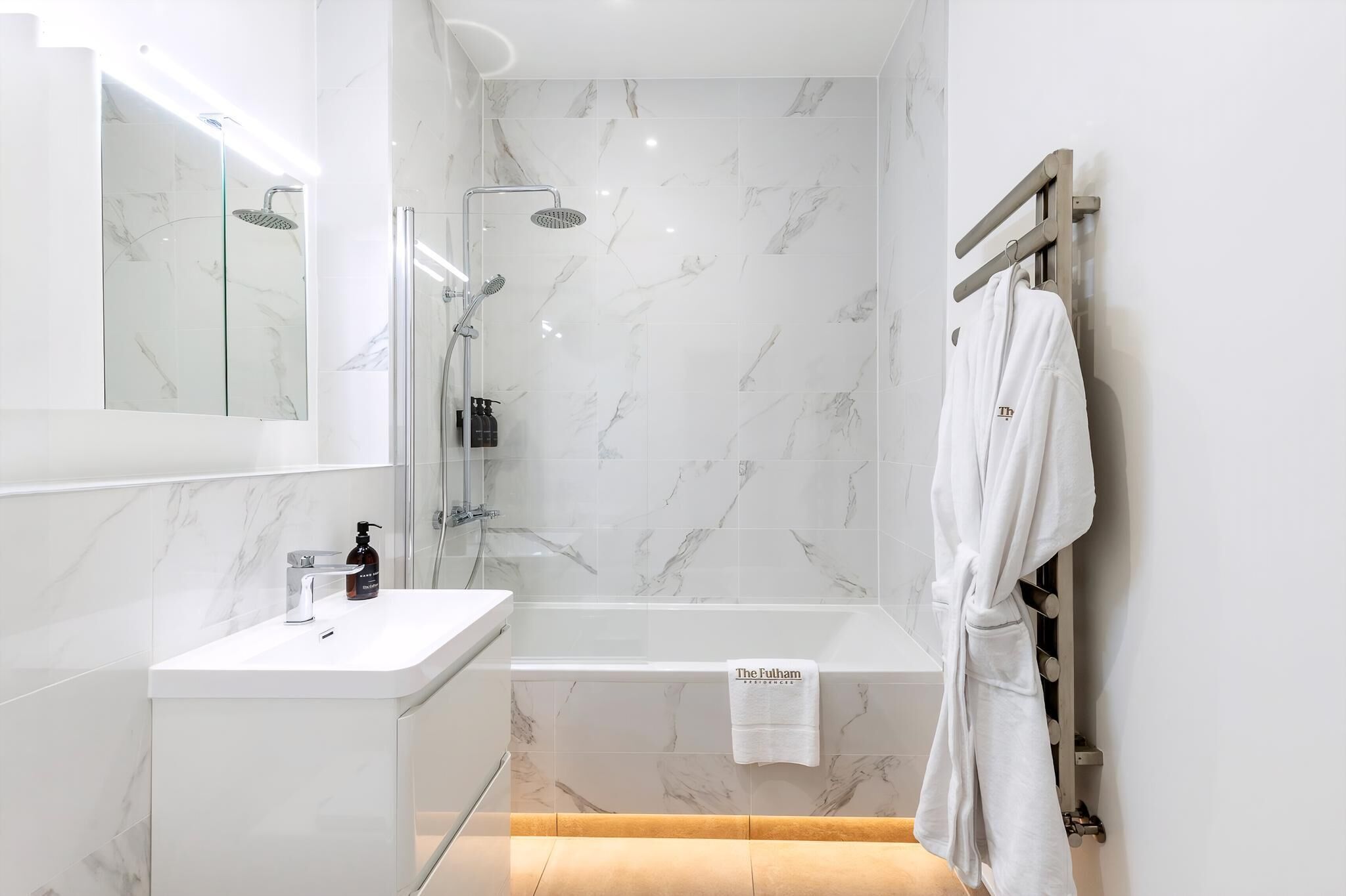 A modern bathroom with a glass-enclosed shower, a white vanity with a mirror, and a robe hanging on a rack.