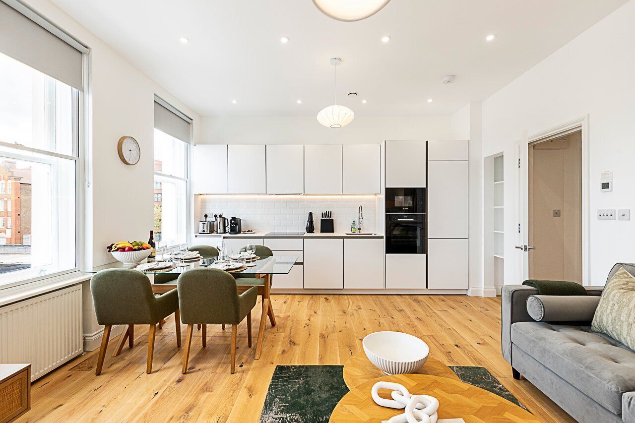 Una cocina moderna con armarios blancos, un comedor con mesa y sillas, y una sala de estar con un sofá.