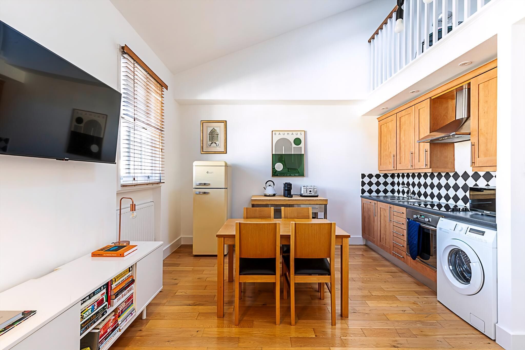 A compact kitchen with a dining area, a washing machine, and a TV mounted on the wall.