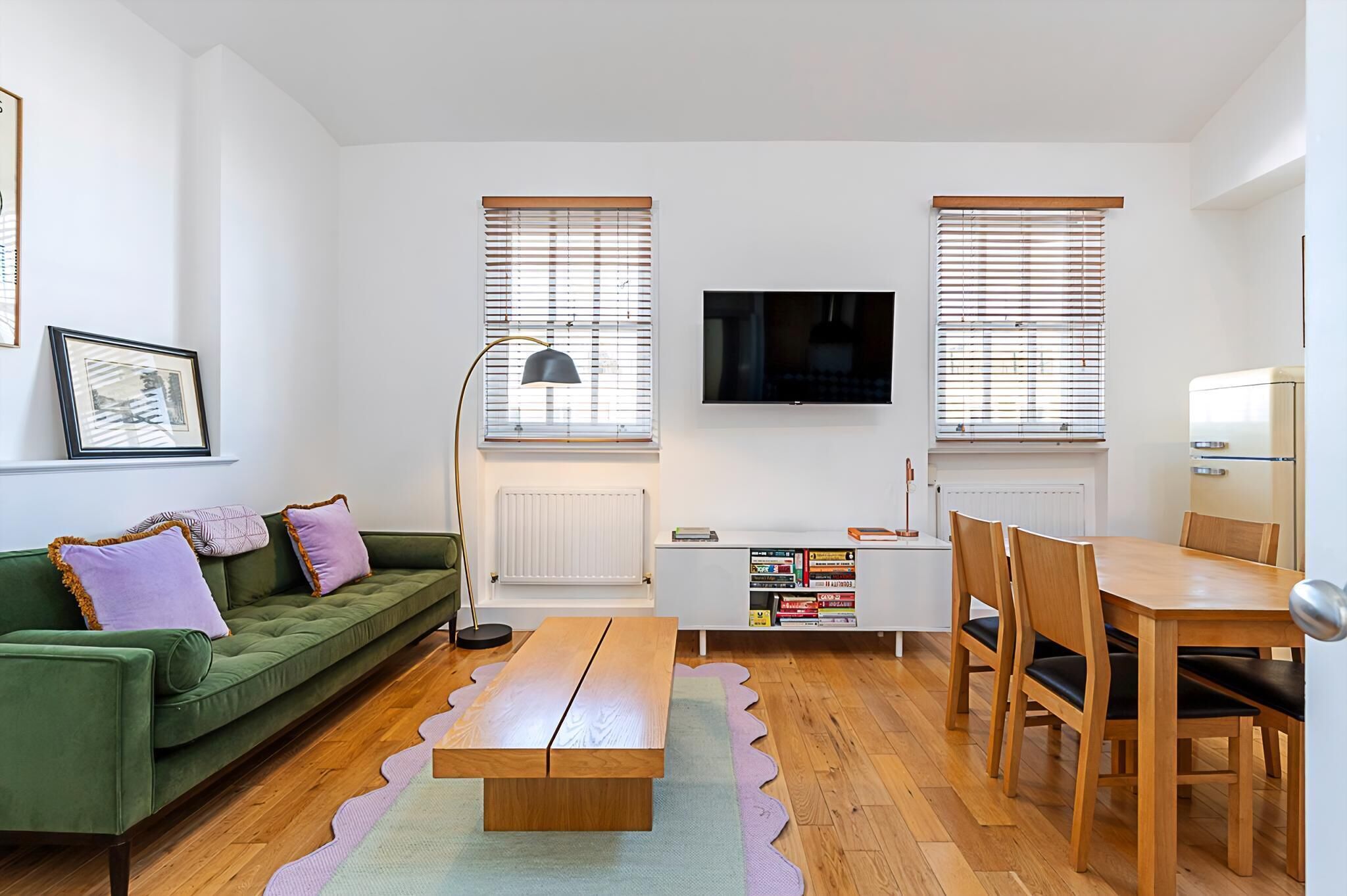 A modern living room with a green sofa, wooden dining table, and a TV mounted on the wall.