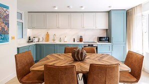 A modern kitchen with light blue cabinets, a wooden dining table with six chairs, and a decorative centerpiece. - 3 Bed In The Heart of Covent Garden (London)