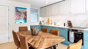 A modern kitchen with teal cabinets, a wooden dining table, and a poster of London. - 3 Bed In The Heart of Covent Garden (London)