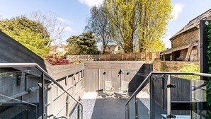 Un espace extérieur moderne avec une terrasse en bois, deux chaises blanches et une balustrade en verre.