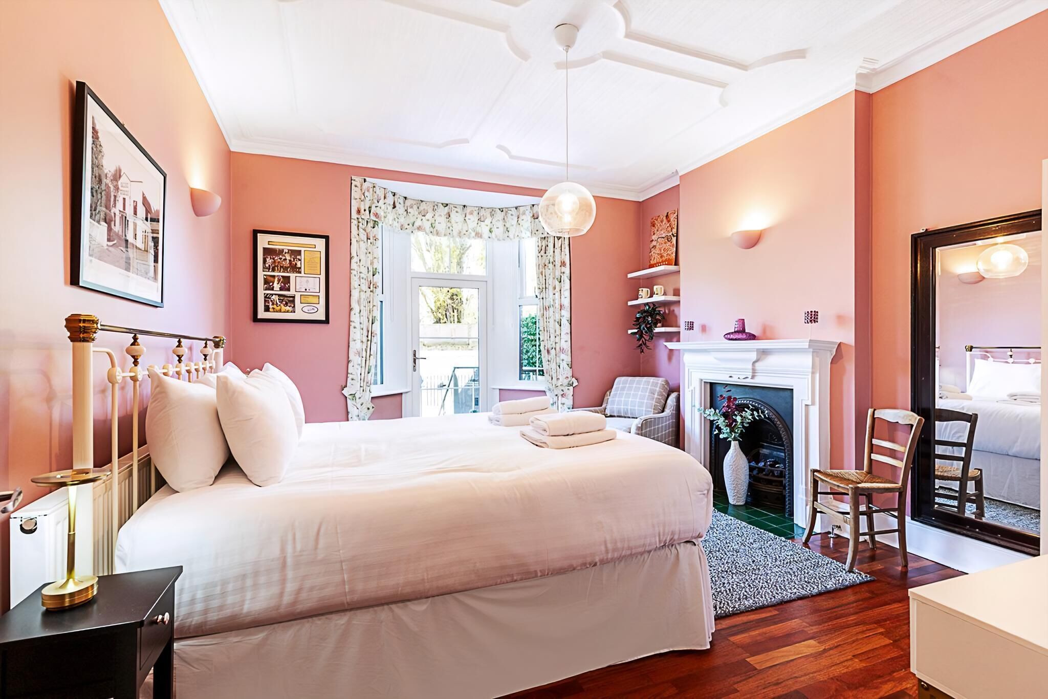 Une chambre à coucher avec un grand lit, une cheminée, un fauteuil et un miroir.