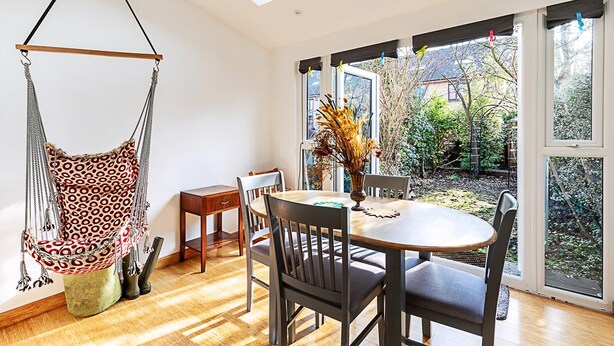 Un espace repas comprenant une table ronde, des chaises, un fauteuil suspendu et une vue sur le jardin grâce à de grandes fenêtres.