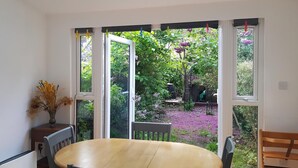Une pièce avec une table ronde, des chaises, un radiateur et une fenêtre donnant sur un jardin.