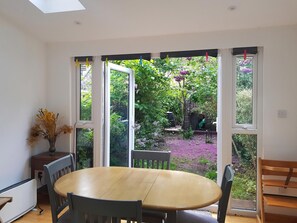 Una habitación con una mesa redonda, sillas, un radiador y una ventana con vistas a un jardín.