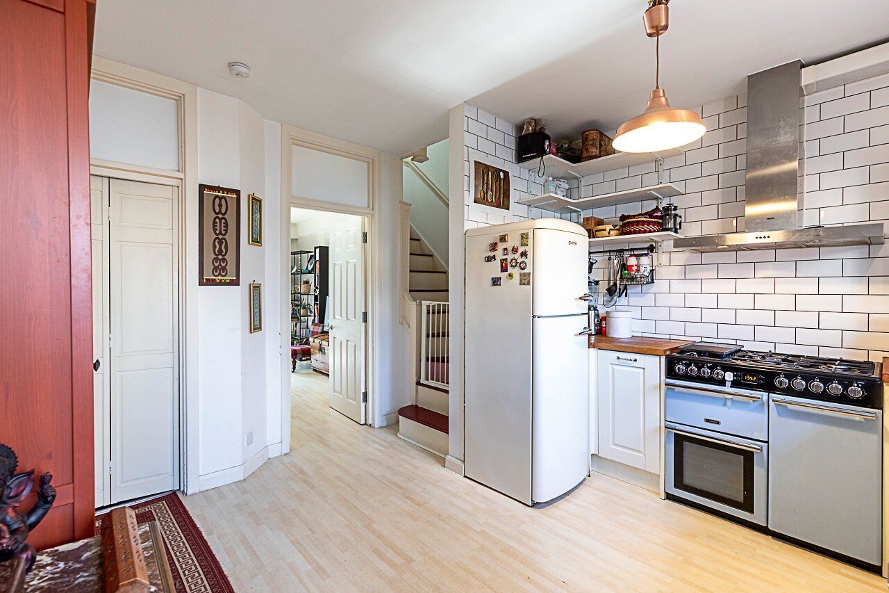 A kitchen with a refrigerator, stove, and oven, a staircase, and a door leading to another room.