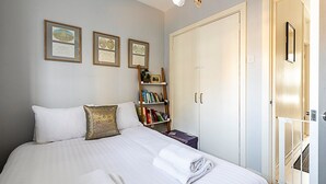 Un lit bien fait, avec du linge de lit blanc, une petite bibliothèque remplie de livres et des certificats encadrés accrochés au mur.