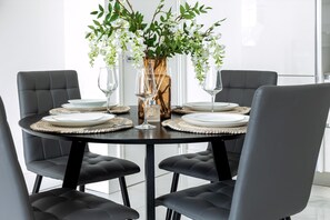 Een ronde eettafel met vier stoelen, een vaas met witte bloemen en wijnglazen.