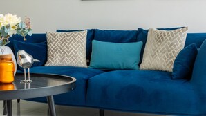 Ein blaues Sofa mit gemusterten Kissen, ein kleiner Tisch mit Kerze und Glas, und eine Vase mit Blumen.