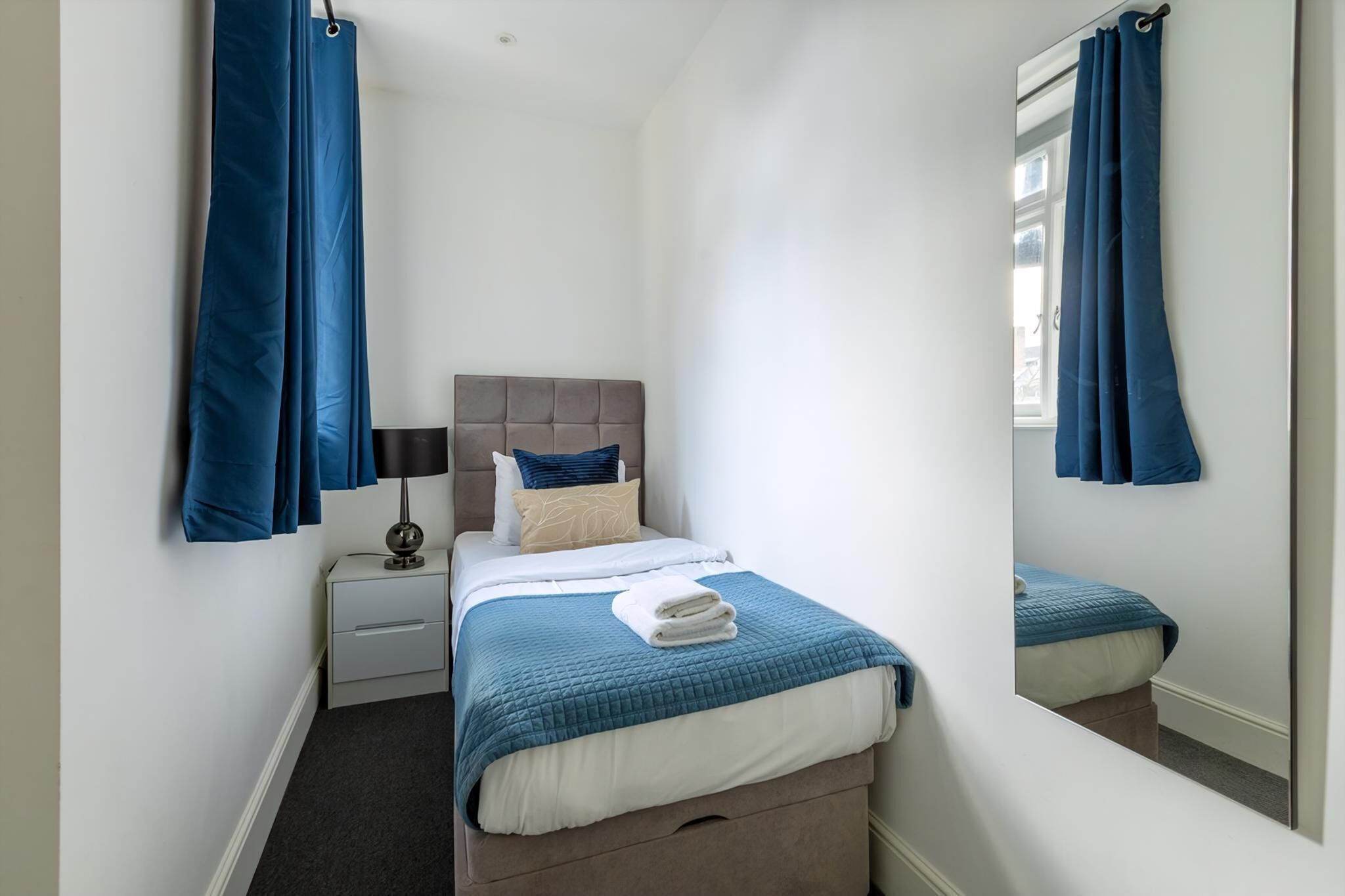 A bedroom with a bed, nightstand, lamp, and a mirror.