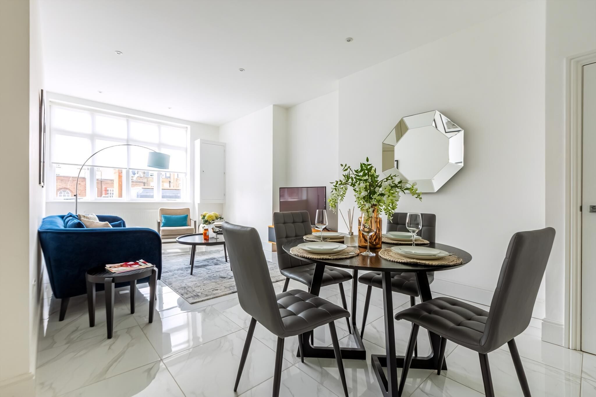 Un espace repas moderne avec une table ronde, des chaises noires et un miroir hexagonal accroché au mur.