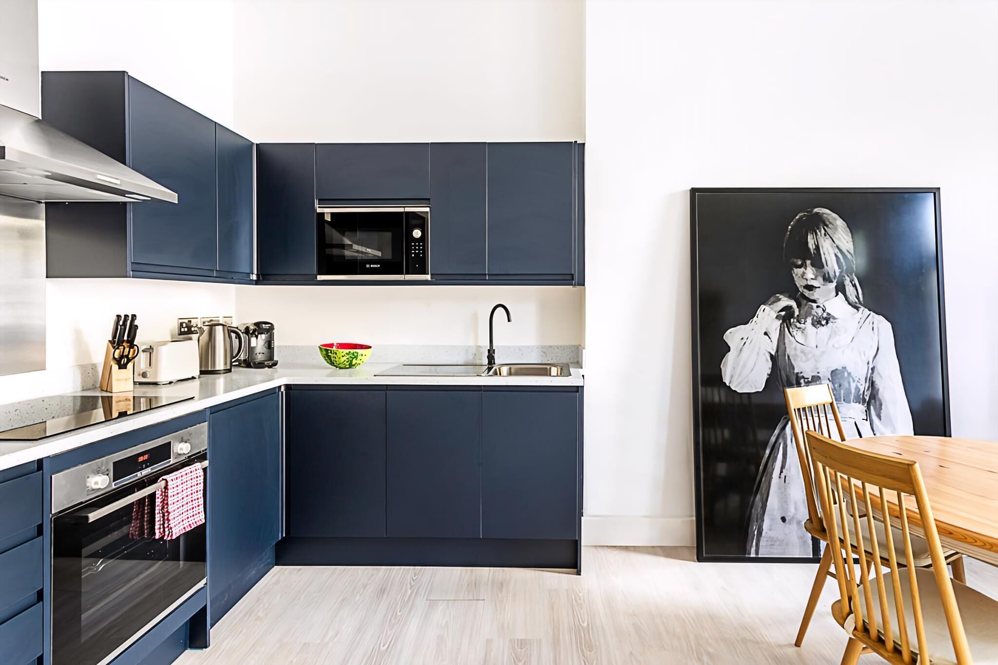 Een moderne keuken met donkere kastjes, een magnetron, een spoelbak en een houten eettafel.