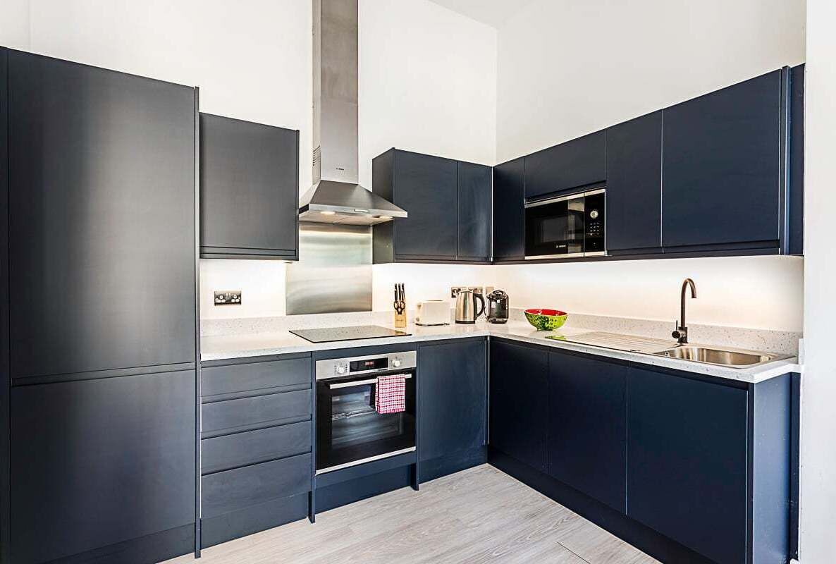 Une cuisine moderne avec des meubles de couleur sombre, des appareils en acier inoxydable et un four encastré.
