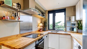 Een moderne keuken met houten aanrechtbladen, geïntegreerde apparatuur en een groot raam met uitzicht op groen.