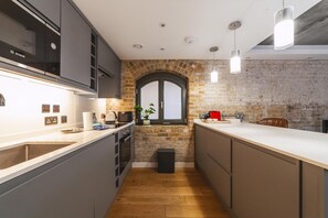 A modern kitchen with a brick wall, a window, and a wooden floor. - Industrial-chic Flat Near Tower Bridge (London)