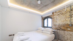 A modern bedroom with a large bed, white linens, a brick wall, and a skylight.