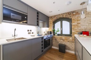 A modern kitchen with grey cabinetry, a Bosch microwave, a sink, and a brick wall. - Industrial-chic Flat Near Tower Bridge (London)