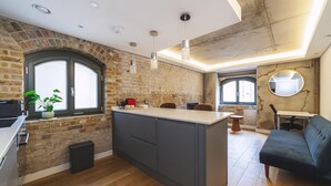 A modern kitchen with a central island, exposed brick walls, and a large window.