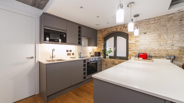 A modern kitchen with grey cabinets, a white countertop, a built-in oven, and a large island.